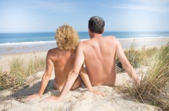 Ein nackter Mann und eine nackte Frau sitzen am Sandstrand.